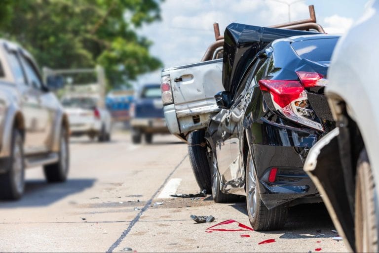 A multi-car pileup on a highway featuring a black sedan with heavy rear-end damage and shattered taillights.