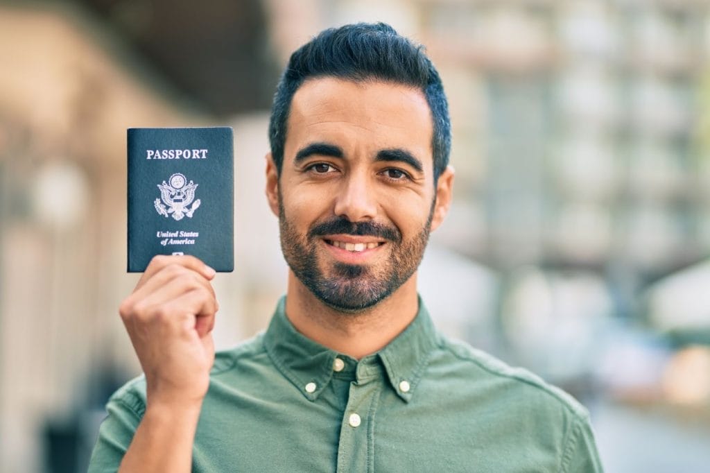 Hispanic man smiling and holding a United States passport.